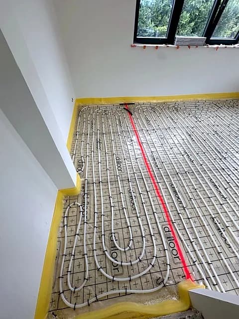 Tubes de chauffage par le sol en cours de pose le long d'un mur